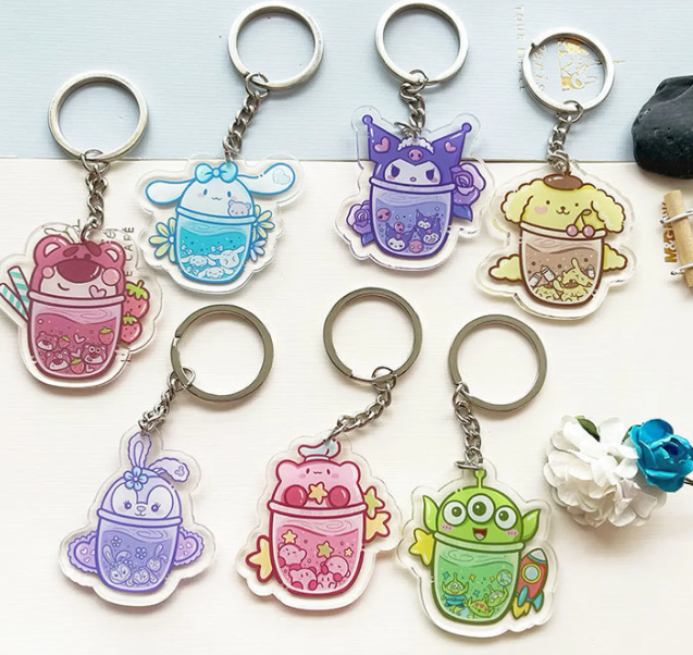 Seven cute and colorful cartoon character custom acrylic keychains on a white table, all connected to shiny round metal split rings